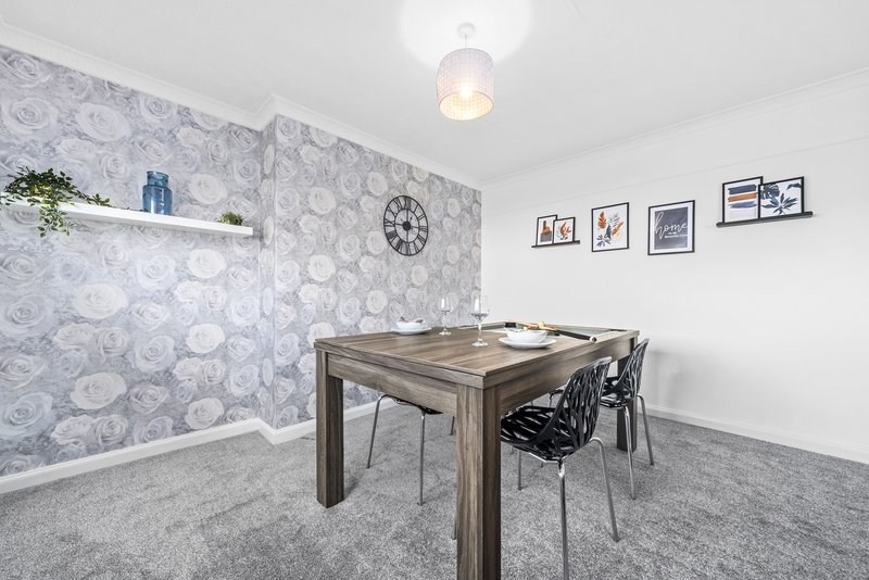 Home office with wooden desk, black chair, patterned wallpaper and wall art