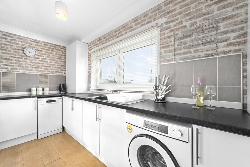 Modern kitchen with white cabinetry, black countertop, washing machine and brick feature wall