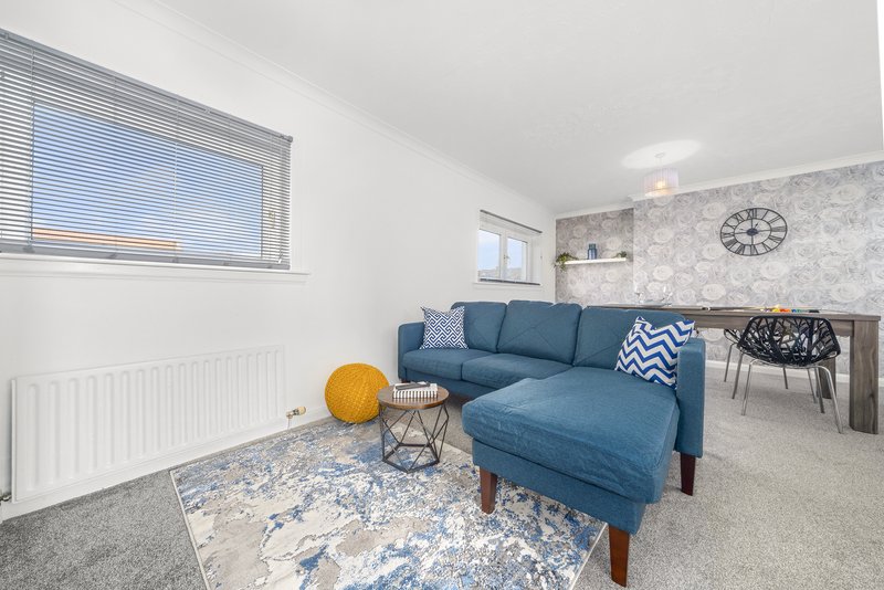Modern living room with blue corner sofa, patterned rug, orange poufs and wall clock