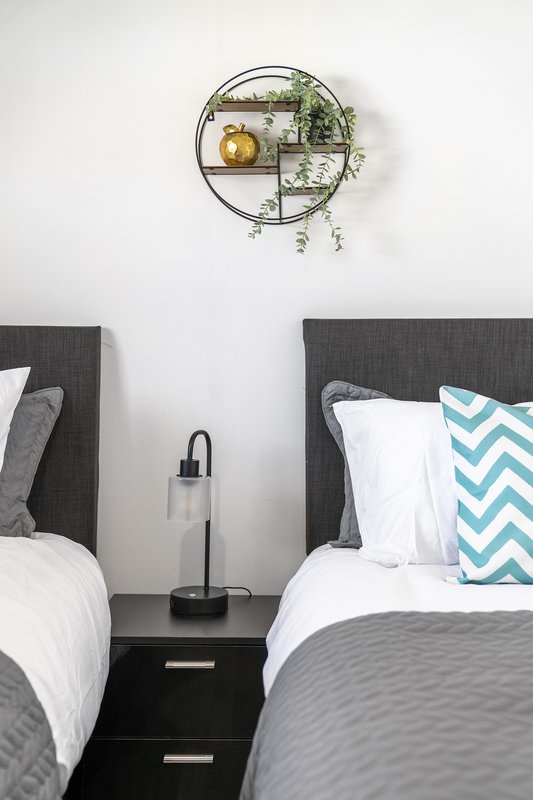 Twin bedroom with dark headboards, white bedding, turquoise cushion, and circular wall shelf with plants