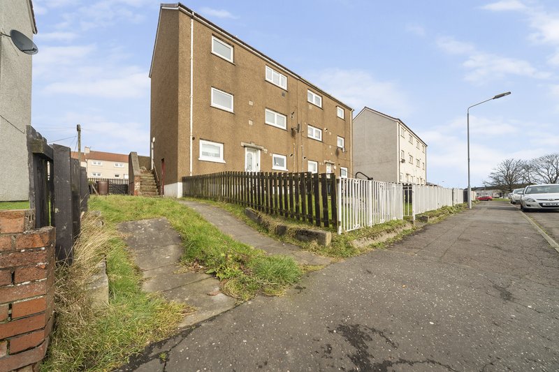 Exterior view of multi-story residential building with driveway and fenced grounds