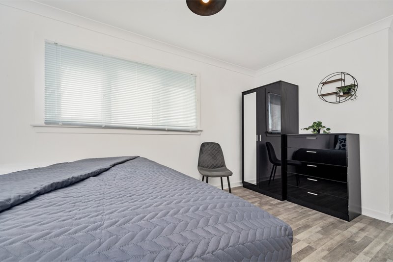 Bedroom with two beds, black wardrobe, dresser, chair and window with blinds