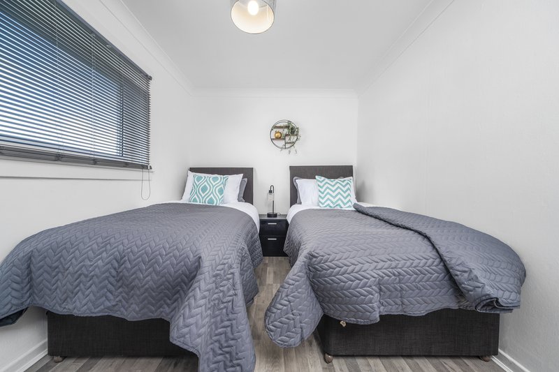 Small bedroom with two single beds, gray quilted bedding, white pillows, window with blinds