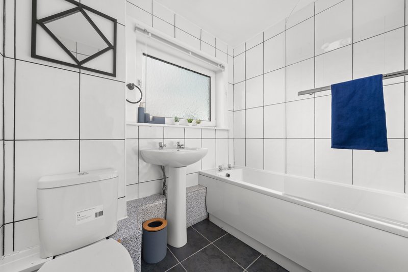 Modern bathroom with white tiles, pedestal sink, toilet, bathtub and blue towel