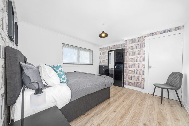 Modern bedroom with double bed, grey headboard, bookshelf wall, wooden floor and pendant light