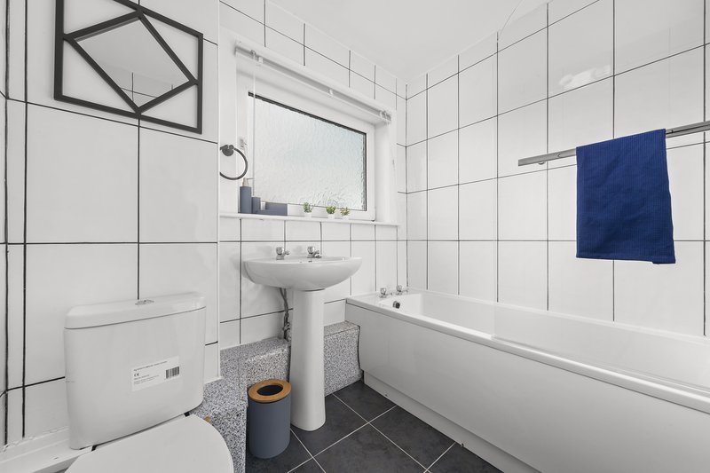 Modern bathroom with white tile walls, pedestal sink, toilet, bathtub and blue towel