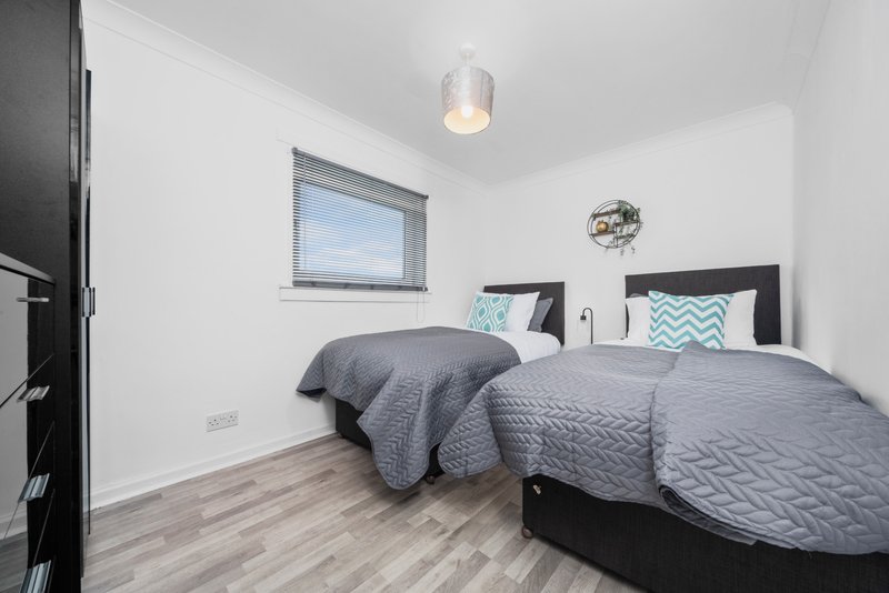 Modern bedroom with two single beds, grey quilts, wooden flooring and window