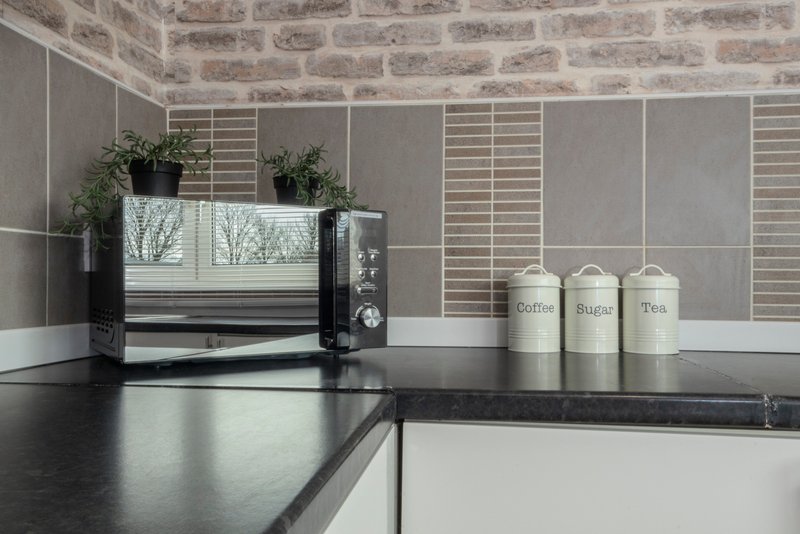Modern kitchen countertop with black worktop, toaster, potted plants, and ceramic storage jars