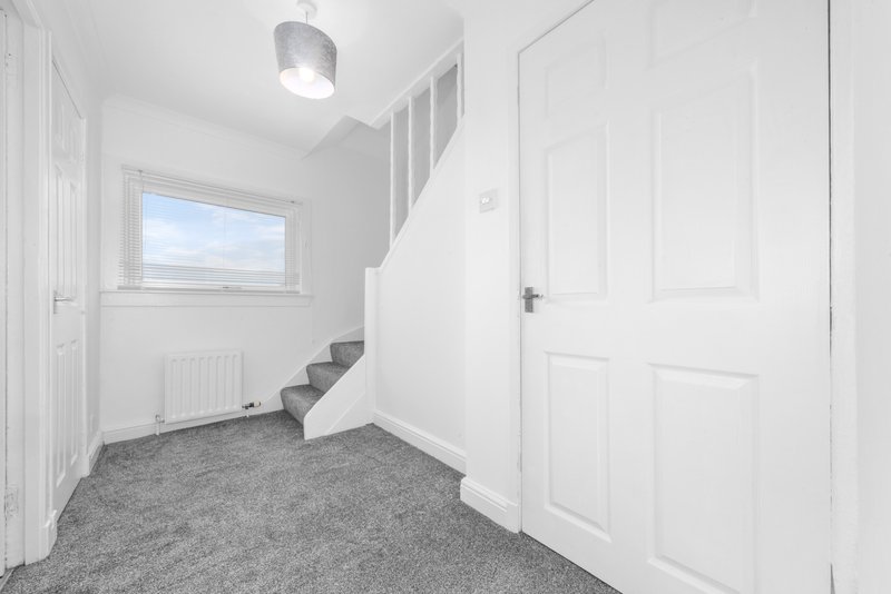 Bright hallway with staircase, gray carpet, white walls and ceiling light fixture