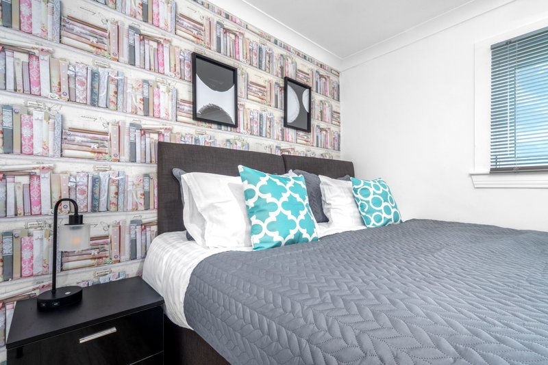 Bedroom with double bed, turquoise patterned cushions, grey quilt, and bookshelf wall