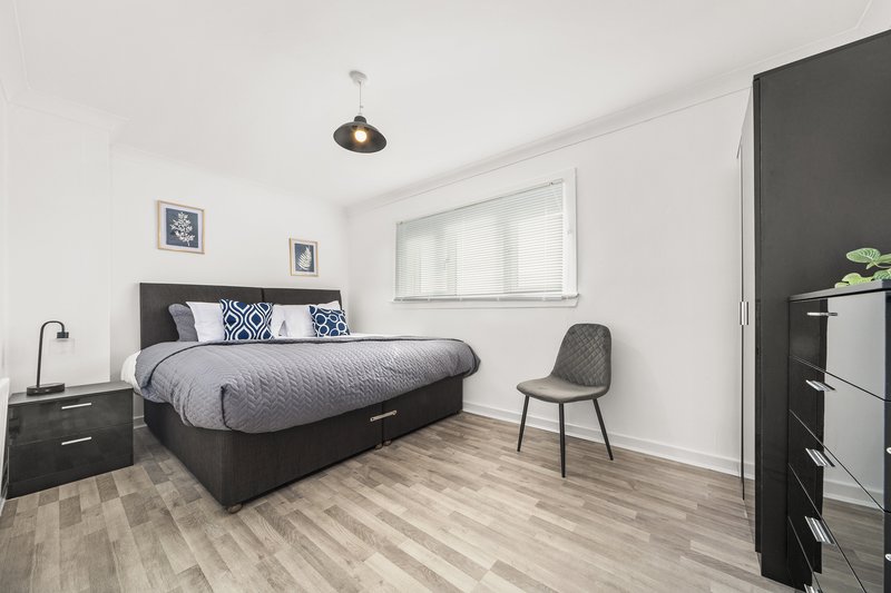 Modern bedroom with dark bed frame, patterned pillows, wooden floor and grey chair