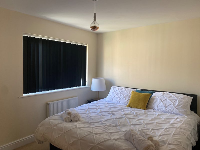Bedroom with double bed, patterned bedding, yellow cushion, pendant light, and window with black blinds