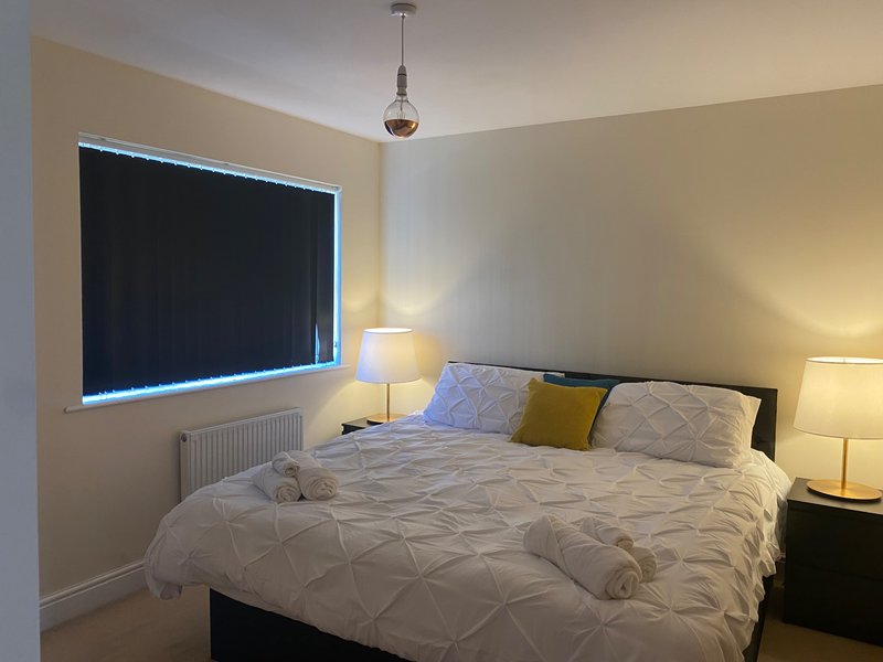 Modern bedroom with super king size bed, white bedding, black headboard, bedside lamps, and wall-mounted window with LED lighting