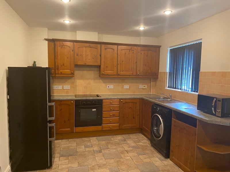 Kitchen with wooden cabinets, black appliances, tiled floor and washing machine