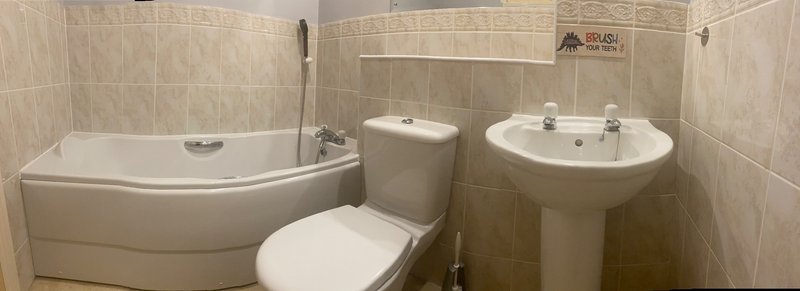 Bathroom with curved bathtub, toilet, pedestal sink and beige tile walls