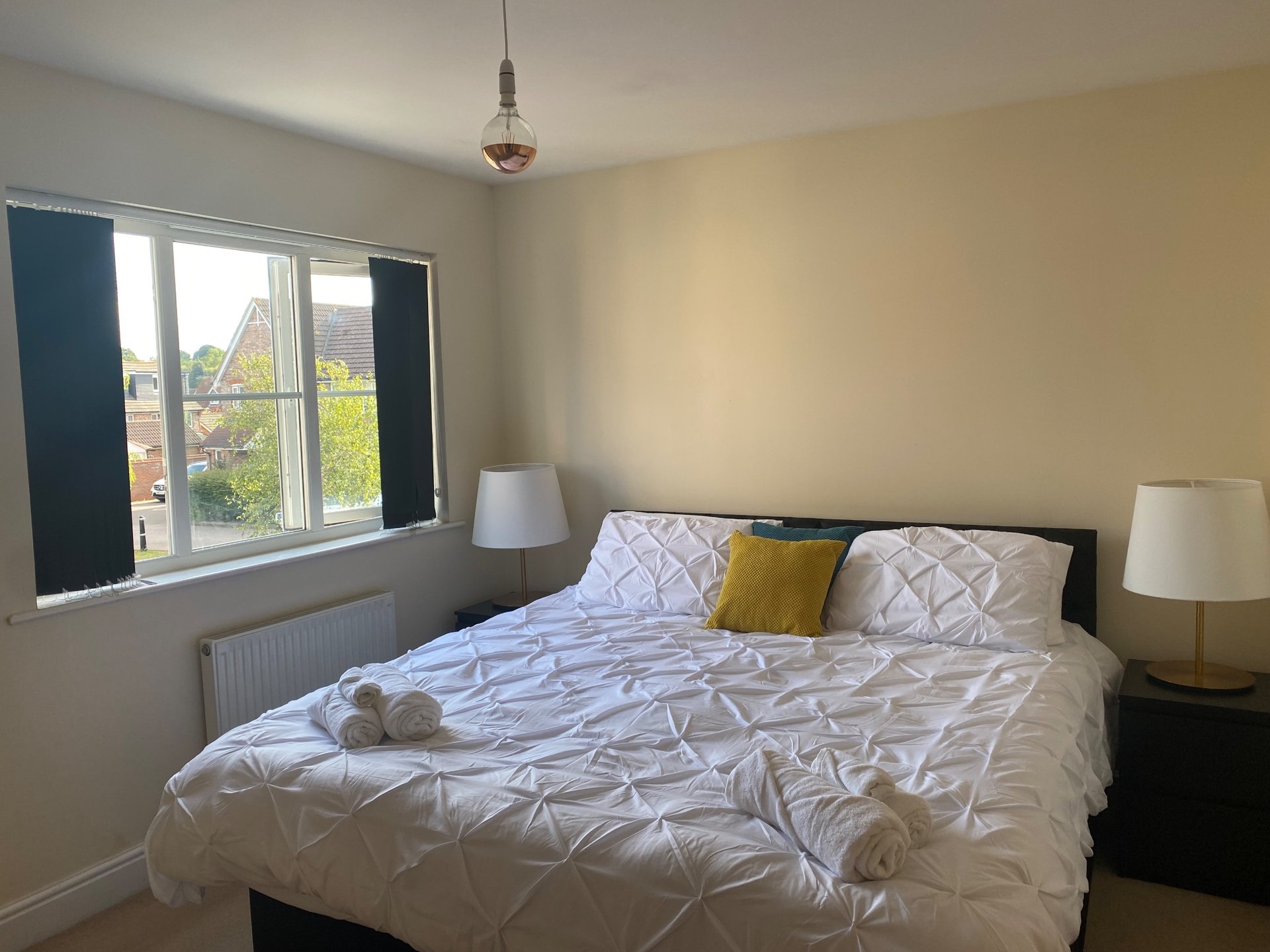 Bedroom with double bed, patterned bedding, bedside lamps, and large window with garden view