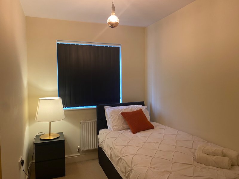 Bedroom with single bed, bedside lamp, window with black vertical blackout blind
