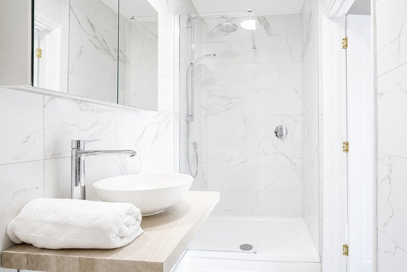 Modern bathroom with marble tiles, vessel sink, mirror, and walk-in shower
