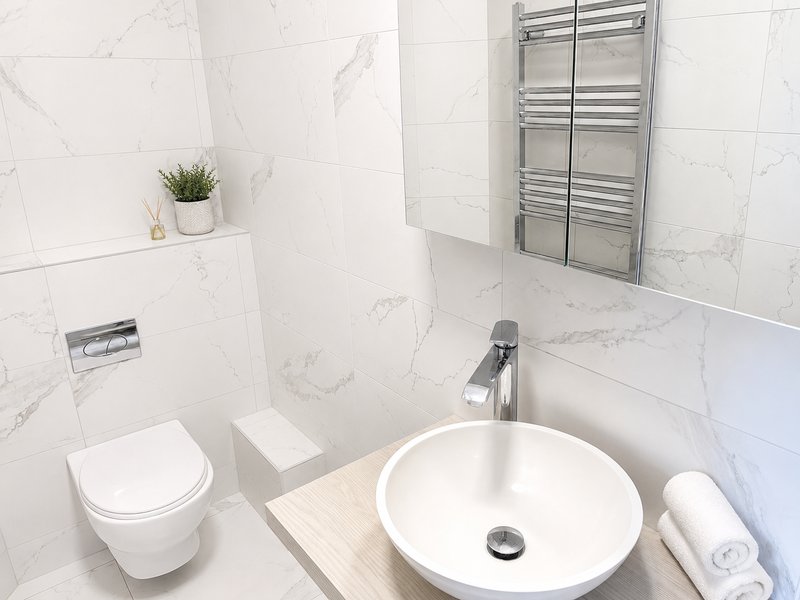 Modern bathroom with white marble tiles, round sink, toilet, heated towel rail and mirror