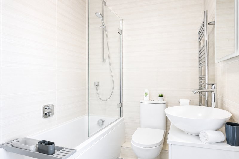 Modern bathroom with white subway tiles, glass shower enclosure, white toilet, and round sink
