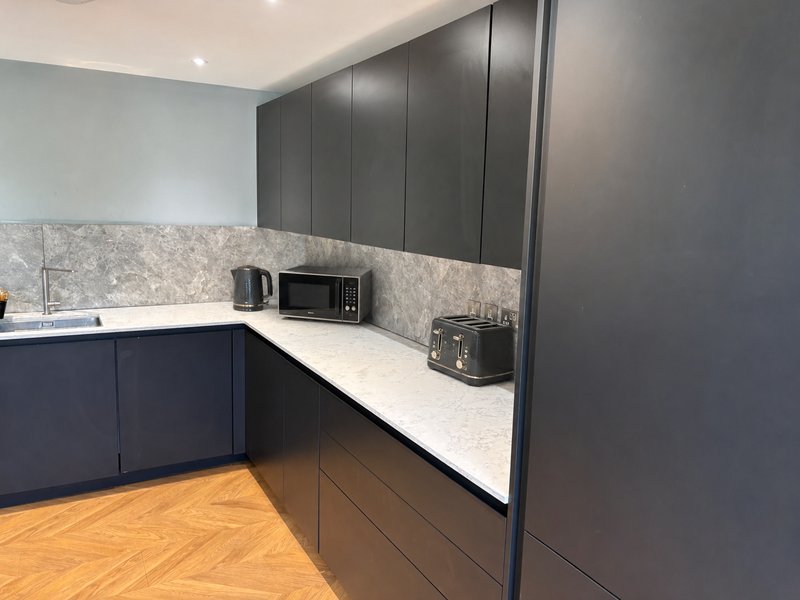 Modern kitchen with dark cabinetry, white countertop, microwave, and wooden flooring