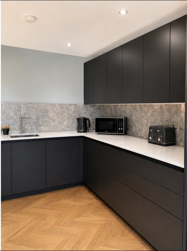 Modern kitchen with black cabinetry, white countertop, stone backsplash and wooden floor
