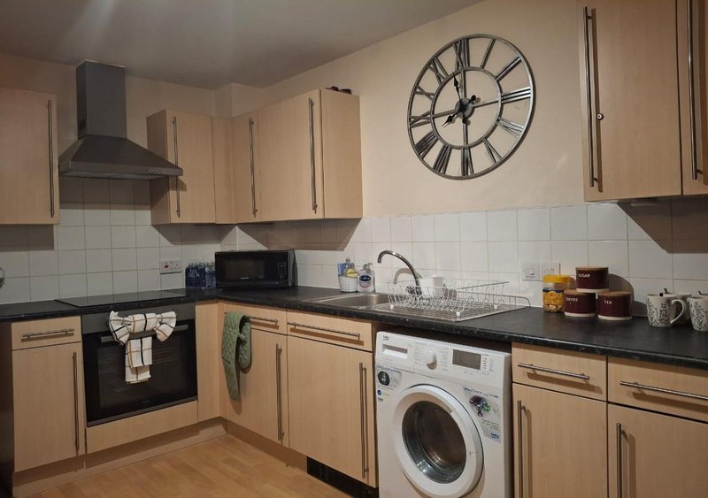 Modern kitchen with wooden cabinets, black countertops, wall-mounted clock and integrated appliances