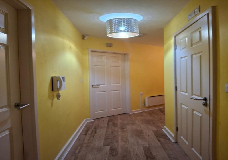 Hallway with yellow walls, multiple white doors, ceiling light fixture and brown flooring