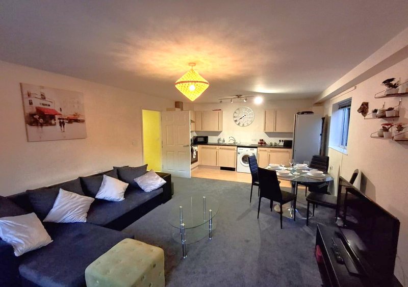 Open-plan living room with dark sofa, dining table, kitchen area and yellow door