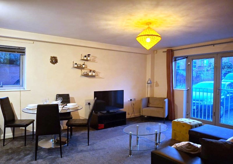Open-plan living area with dining table, TV, armchair, and glass doors to balcony