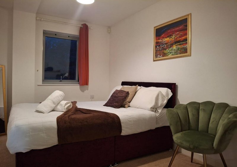 Bedroom with double bed, brown bedding, white pillows, green armchair and framed artwork