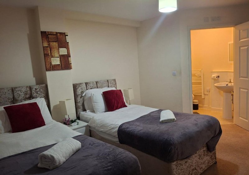Bedroom with two single beds, burgundy and white pillows, bedside tables, and ensuite bathroom visible