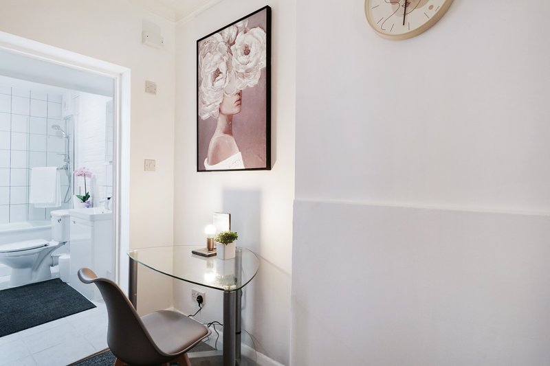 Modern bedroom corner with desk, framed wall art, clock, and open ensuite bathroom door