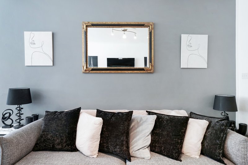 Living room with gray sofa, decorative pillows, wall mirror, framed line drawings, and table lamps
