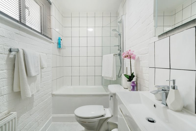Clean white bathroom with toilet, sink, shower and tiled walls