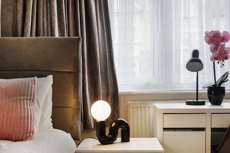 Modern bedroom with upholstered headboard, bedside lamp, pink flowers, and sheer curtains by window
