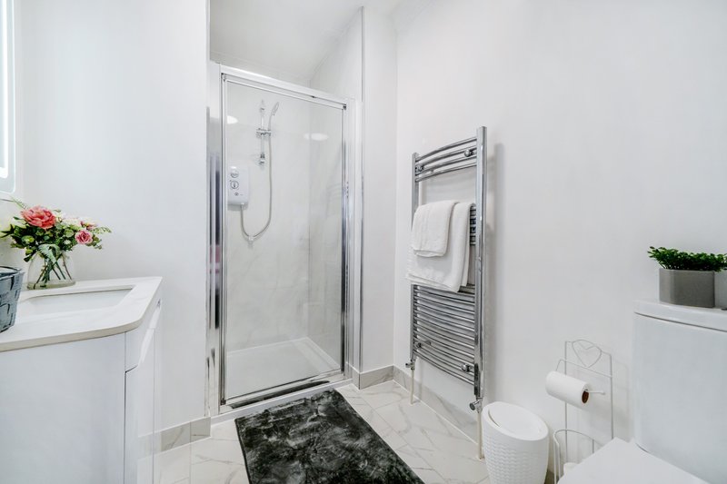 Modern white bathroom with shower enclosure, towel radiator, and sink vanity