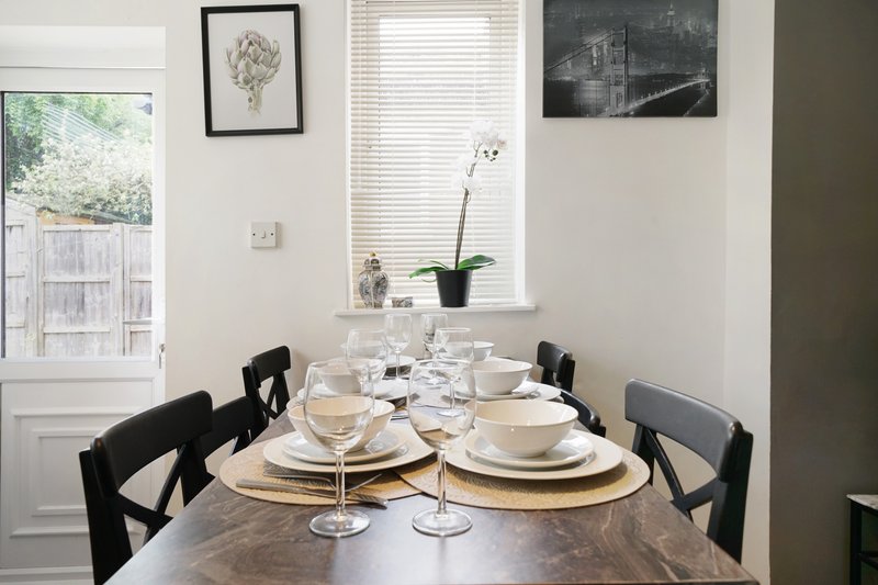 Dining room with set table, black chairs, framed artwork, and garden view window