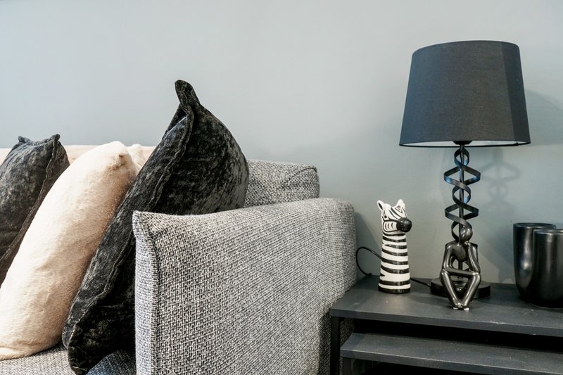 Living room with gray upholstered sofa, decorative cushions, table lamp, and ceramic ornaments