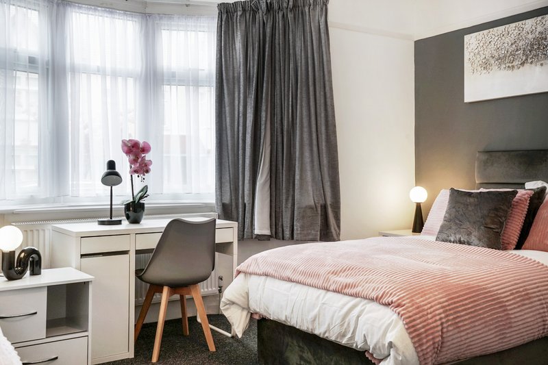Modern bedroom with double bed, desk, chair, grey curtains and window with natural light