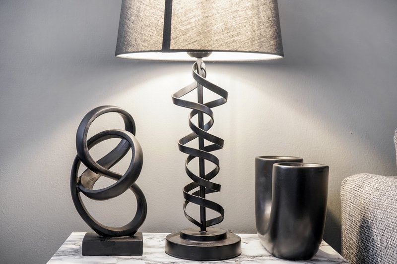Bedside table with decorative sculptures, modern lamp with fabric shade, and vase