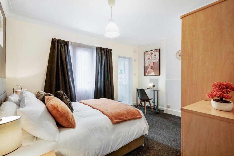 Bedroom with double bed, orange pillows, dark curtains, desk area and wooden wardrobe