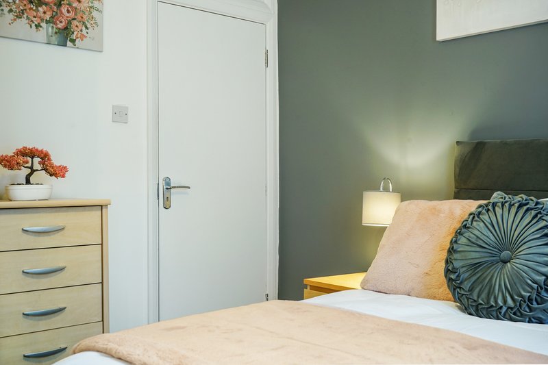 Bedroom with double bed, wooden dresser, green headboard and bedside lamp