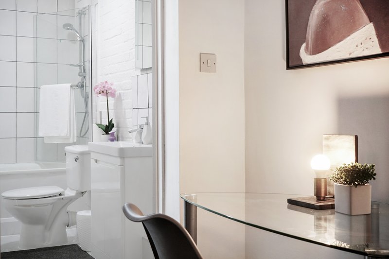 Modern bathroom with white tile walls, shower enclosure, toilet, and vanity sink with flowers
