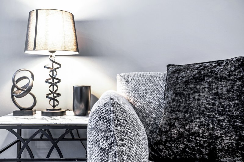 Bedside table with silver lamp, decorative objects, and cushions on bed