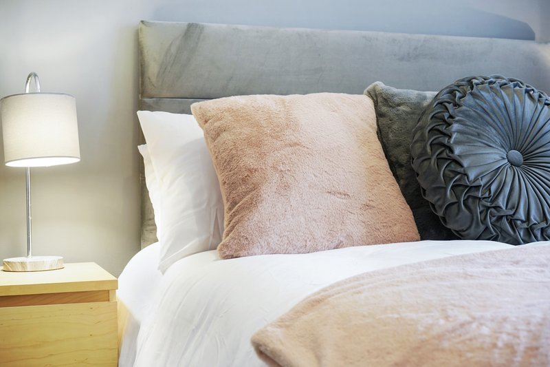 Bedroom with gray upholstered headboard, white bedding, decorative cushions, and bedside lamp