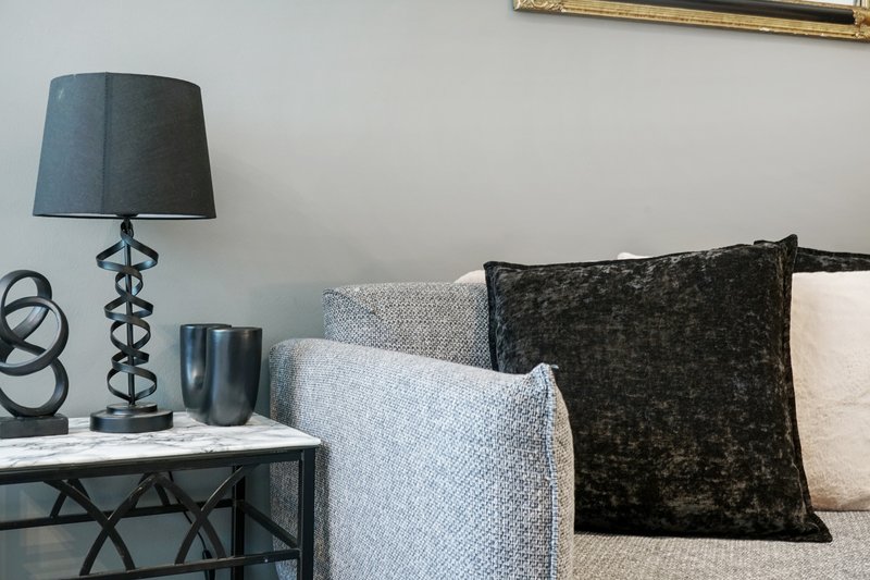 Living room corner with grey sofa, decorative pillows, side table lamp and wall art