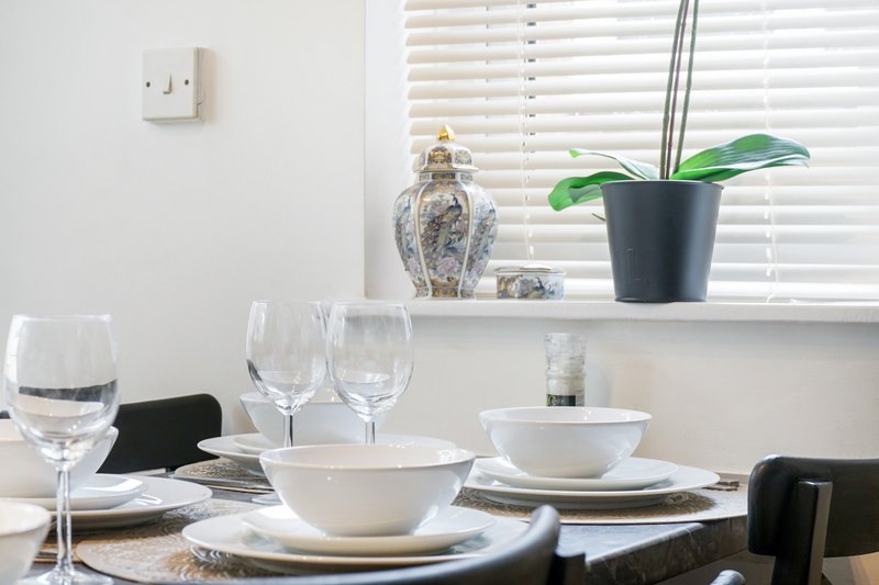 Dining table set with white bowls, glasses, plates and window sill decor