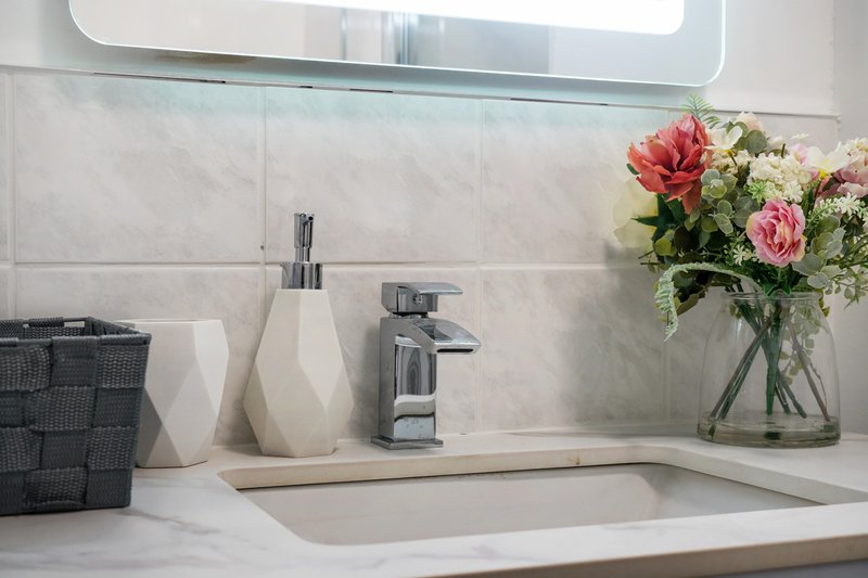 Modern bathroom sink with marble countertop, chrome faucet, soap dispensers and fresh flowers in vase