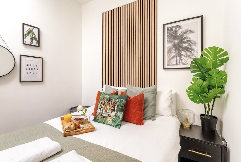 Bedroom with double bed, decorative pillows, wooden headboard, and potted plant